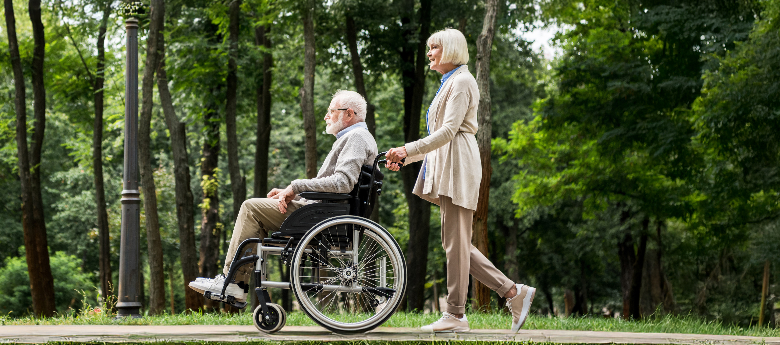 An older lady pushing an older man in a wheel chair on a pathway